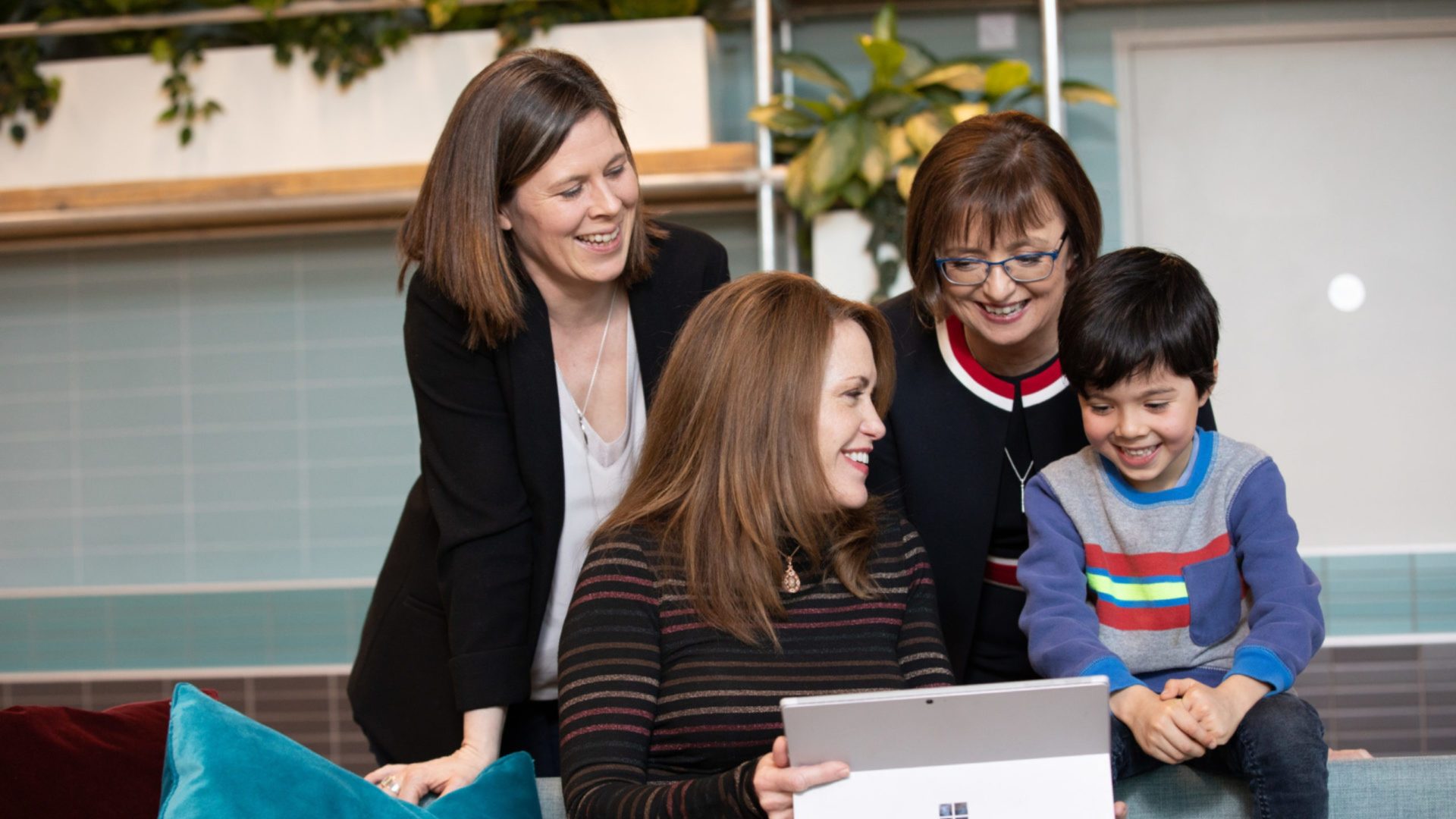 A photo of three women and a boy interacting with a tablet computer.