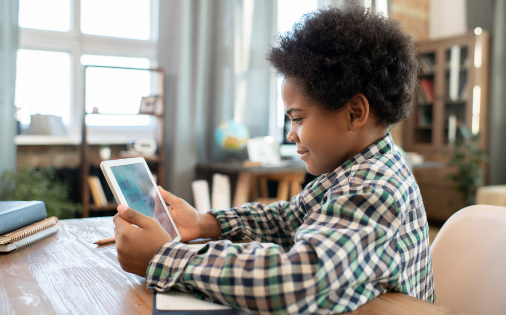 A photo of a young boy sitting at a desk, reading off of an iPad.