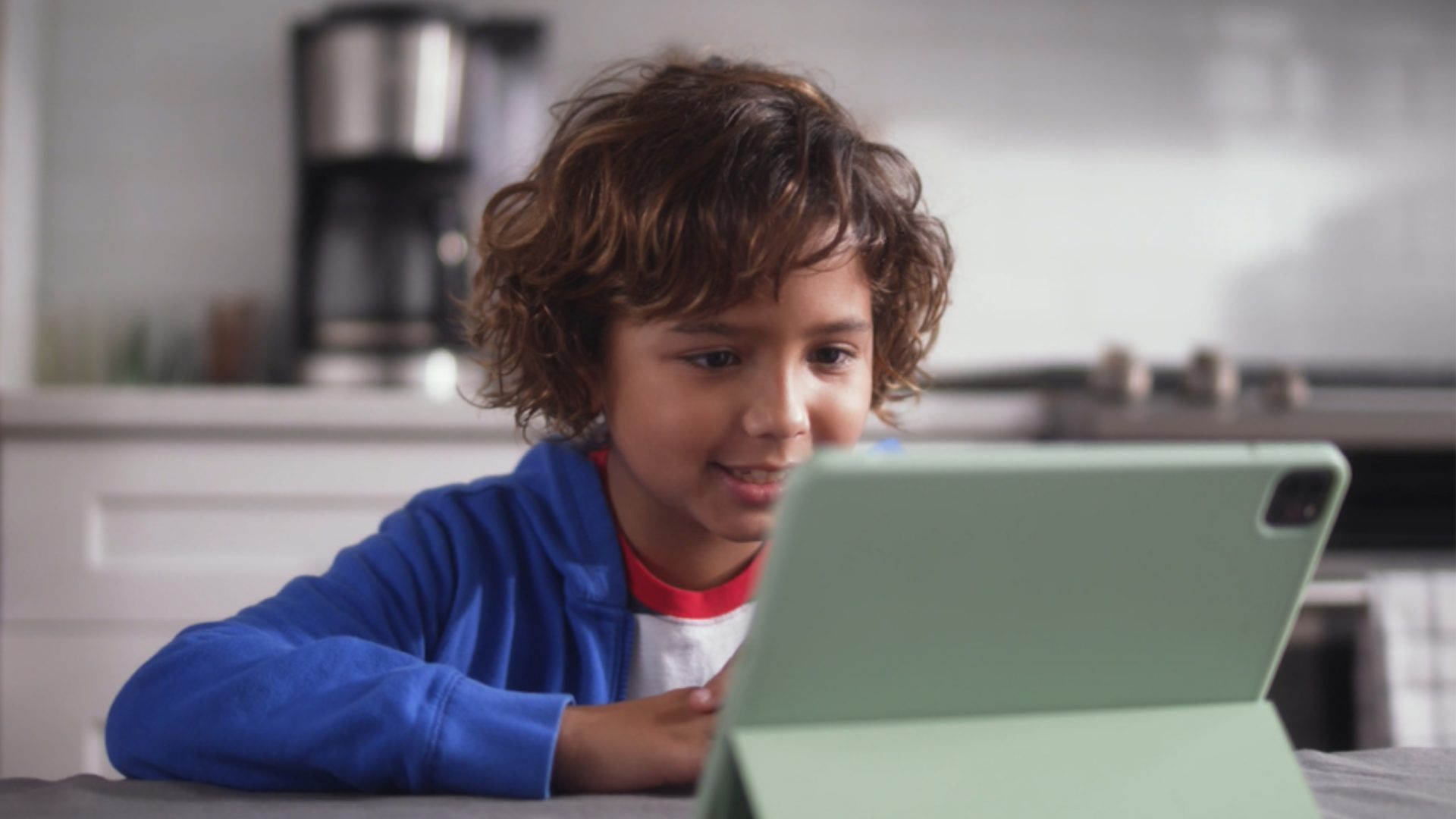 A photo of a boy sitting at a kitchen table talking into a voice-enabled device, powered by speech recognition technology from SoapBox Labs.