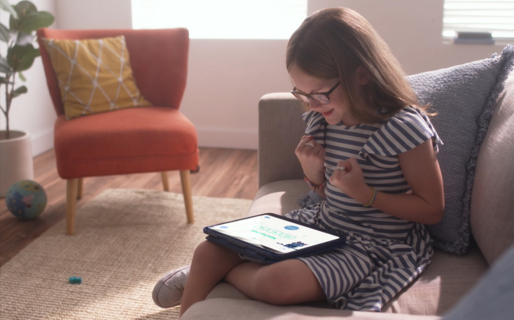 A photo of a young girl sitting on a couch, celebrating after getting a correct answer in a digital reading game.