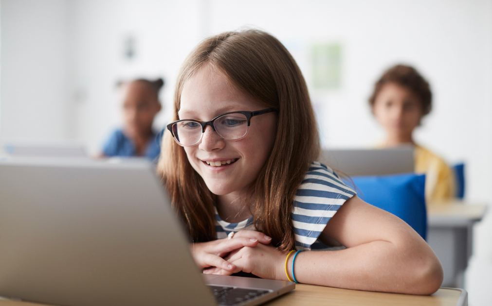 A photo of an eight-year-old girl sitting in class reading off a computer