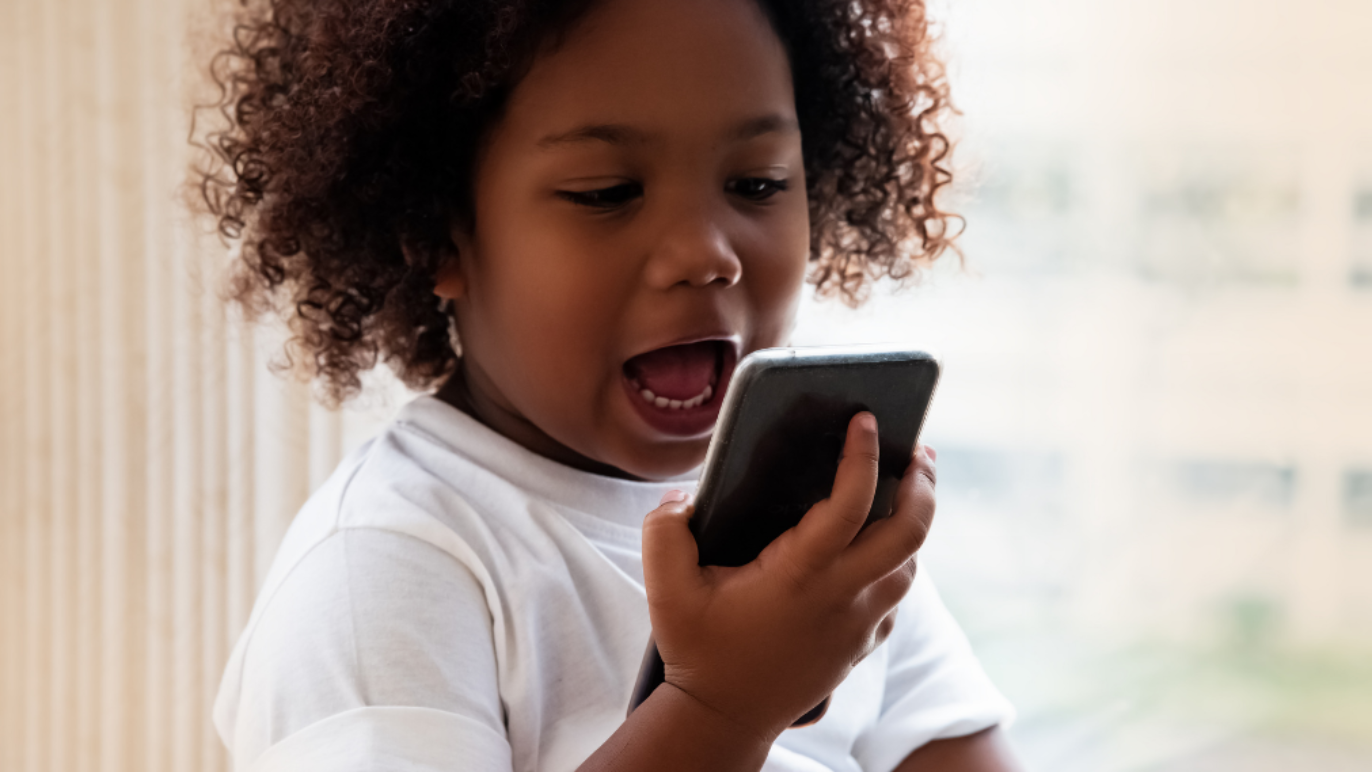 An image of a young girl, about three years old, speaking into a smart phone.