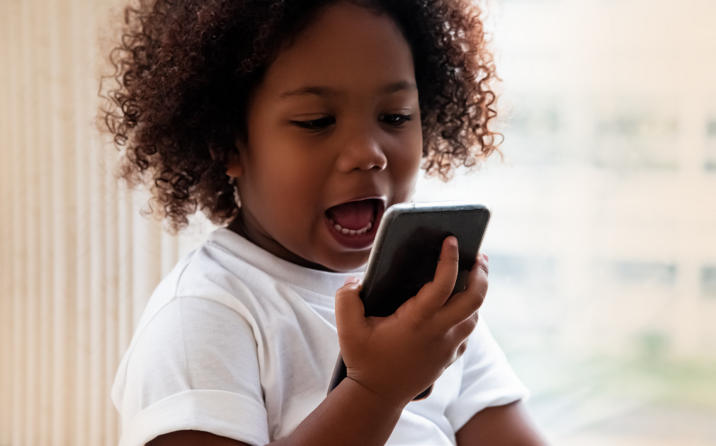 An image of a young girl, about three years old, speaking into a smart phone.