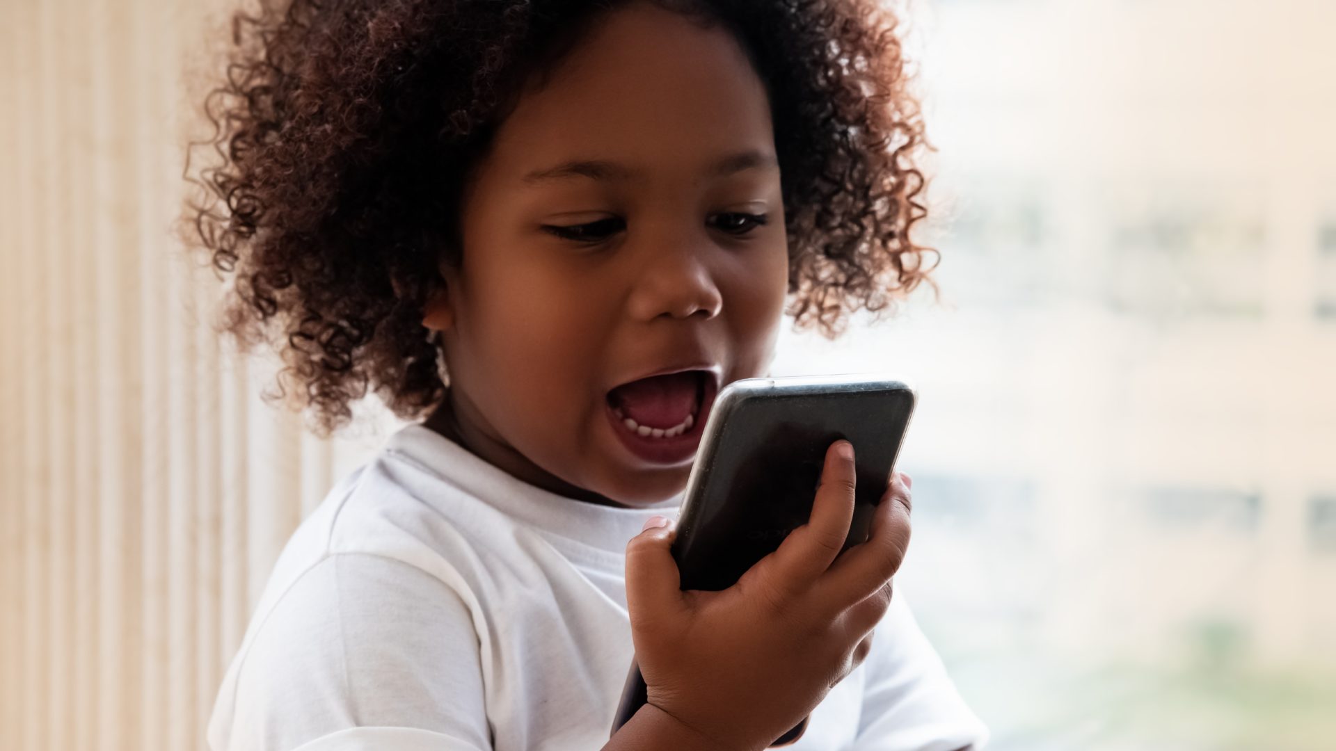 An image of a young girl, about three years old, speaking into a smart phone.