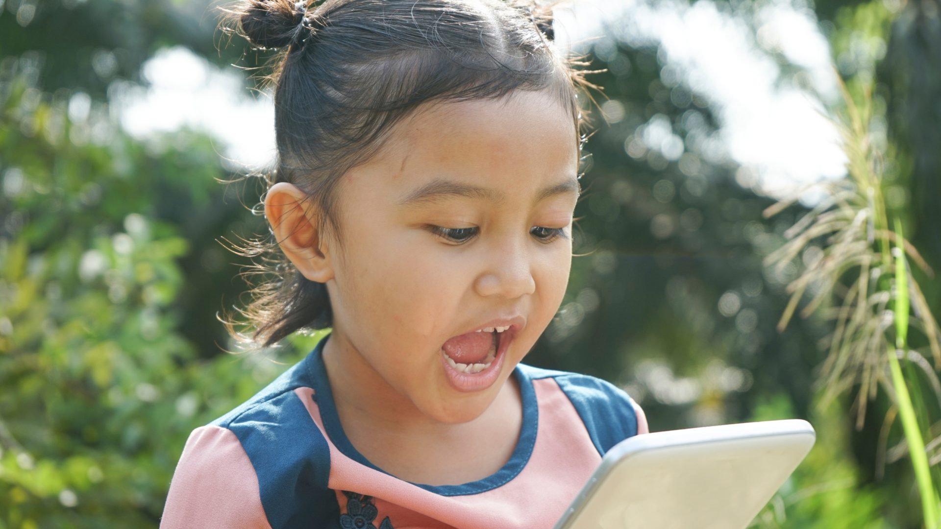 A photo of a young girl standing outside, talking into a smart phone.