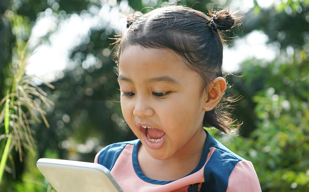 A photo of a young girl standing outside talking into her iPhone.