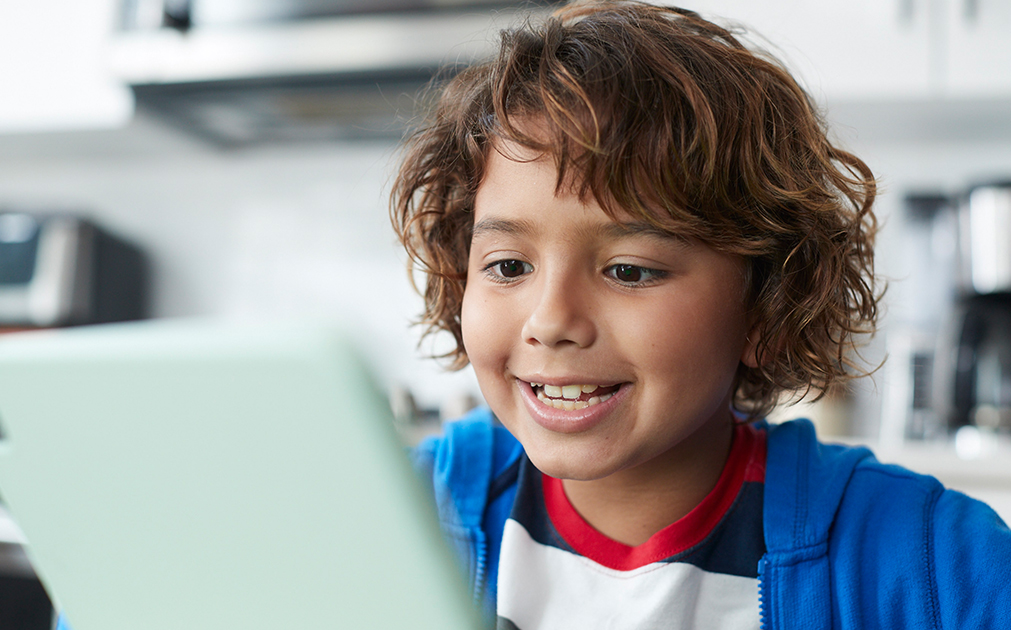 Photo of a young boy sitting at his kitchen table, practicing his reading from an iPad.