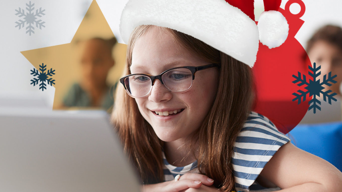 A photo of an eight-year-old girl sitting in a classroom, reading off of an iPad. The girl is wearing a Santa hat.