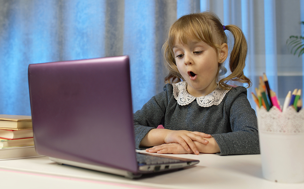 Girl sits at desk speaking into a laptop.