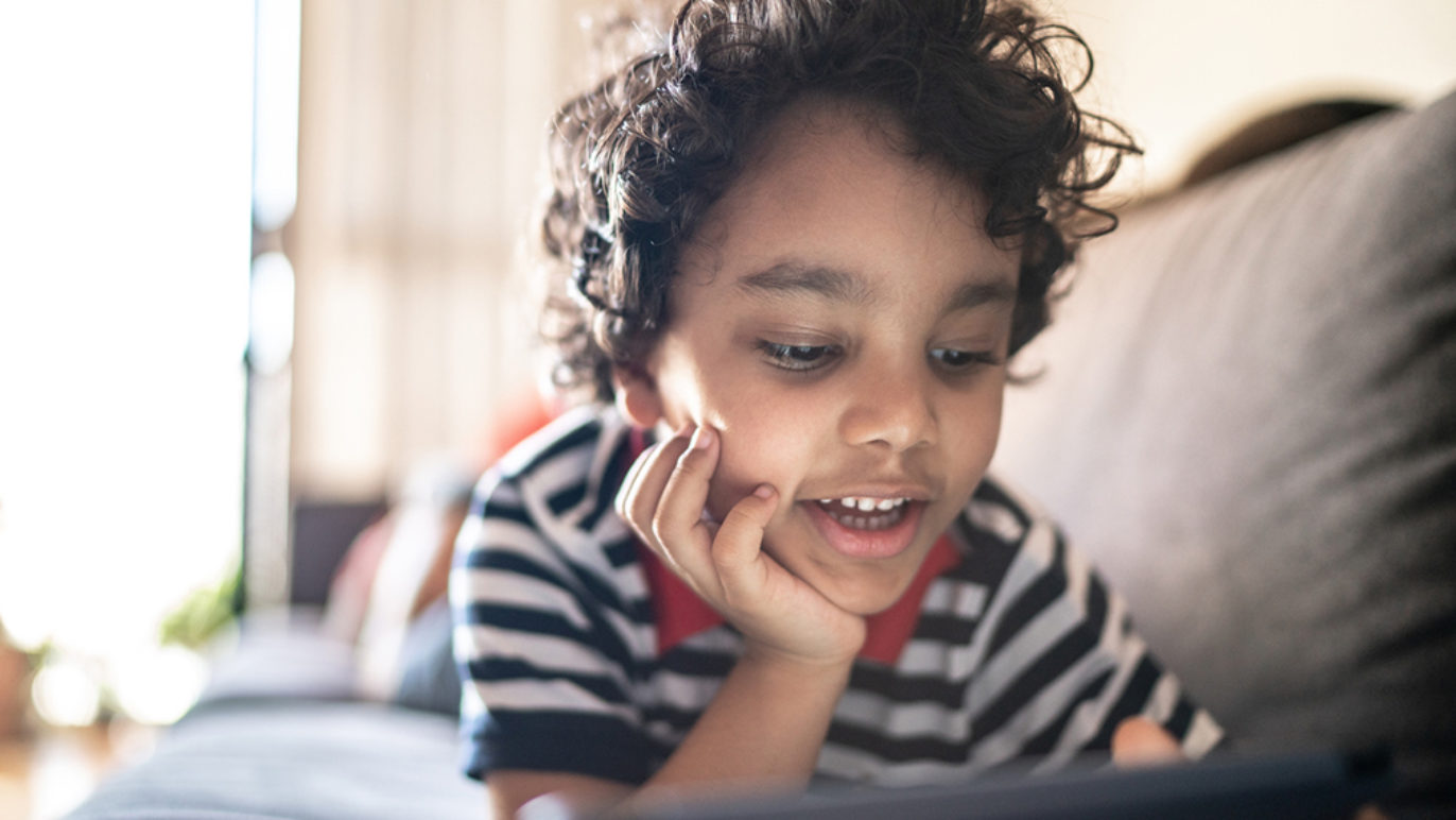 A photo of a boy lying on his couch, talking into an iPad.