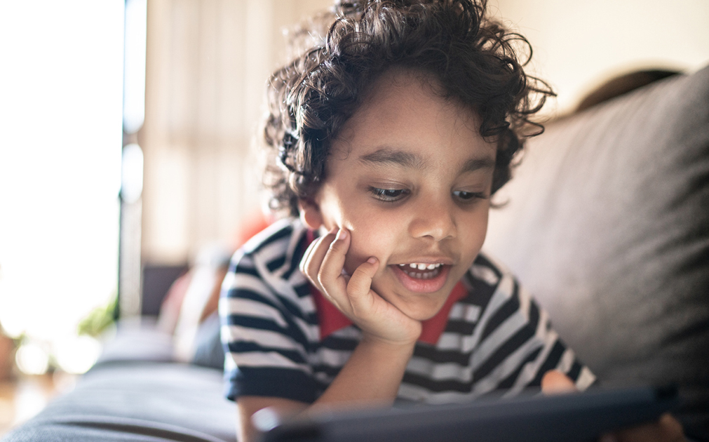 A photo of a boy lying on his couch, talking into an iPad.