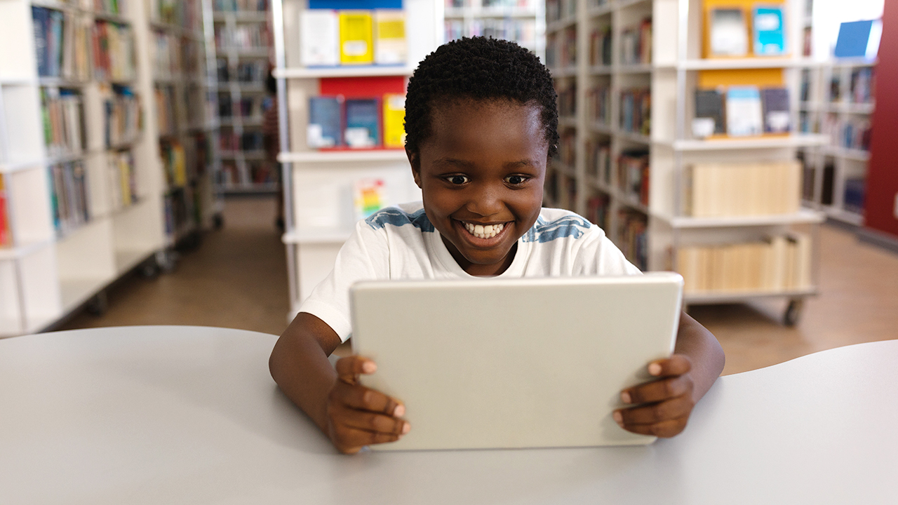 A boy sitting at a desk, talking into a tablet computer.