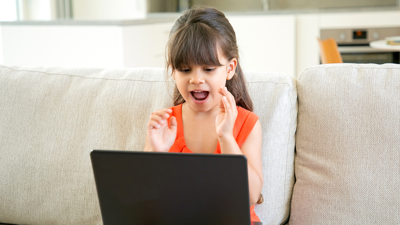 A girl sitting on a couch, talking into a laptop computer.