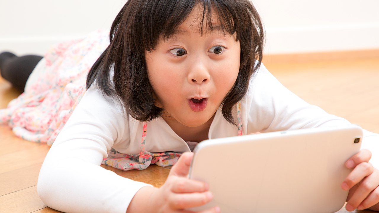 A girl lying on the floor, talking into a tablet computer.