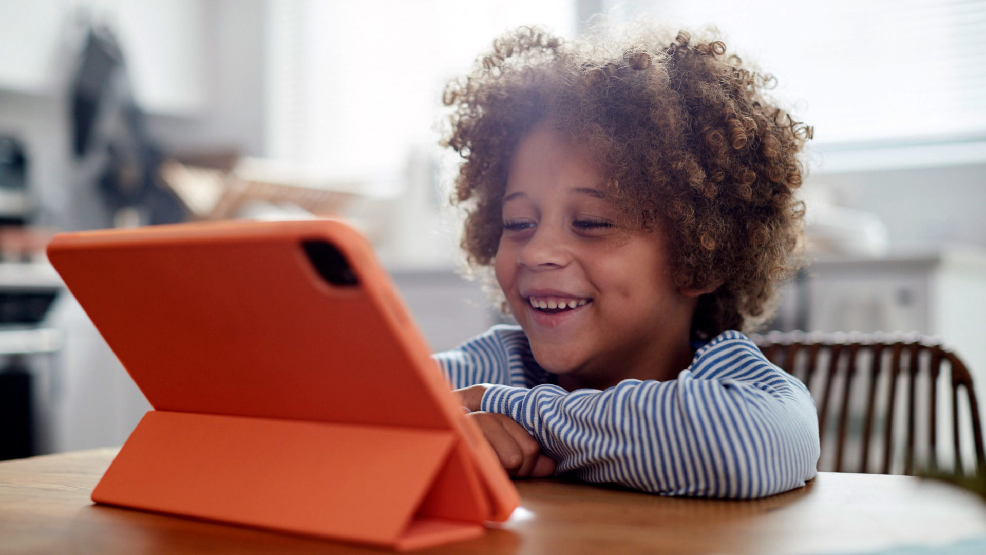 A boy sitting at a kitchen table talking into an iPad.