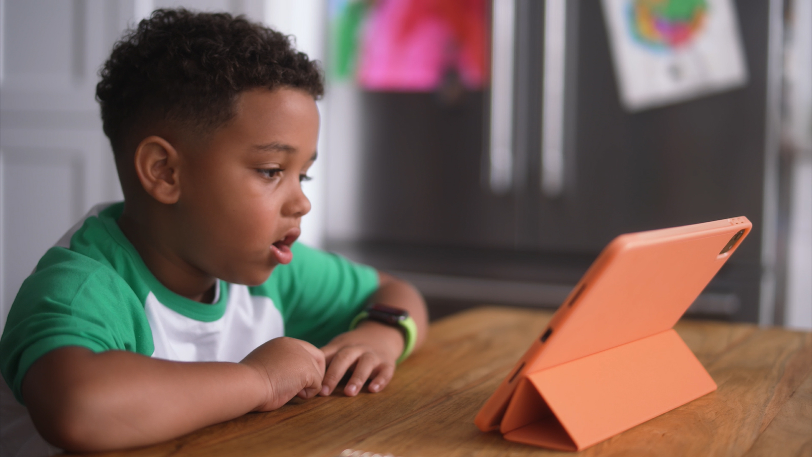 A photo of a six-year-old boy sitting at a kitchen completing a voice-enabled math assessment on his iPad powered by SoapBox's voice technology.