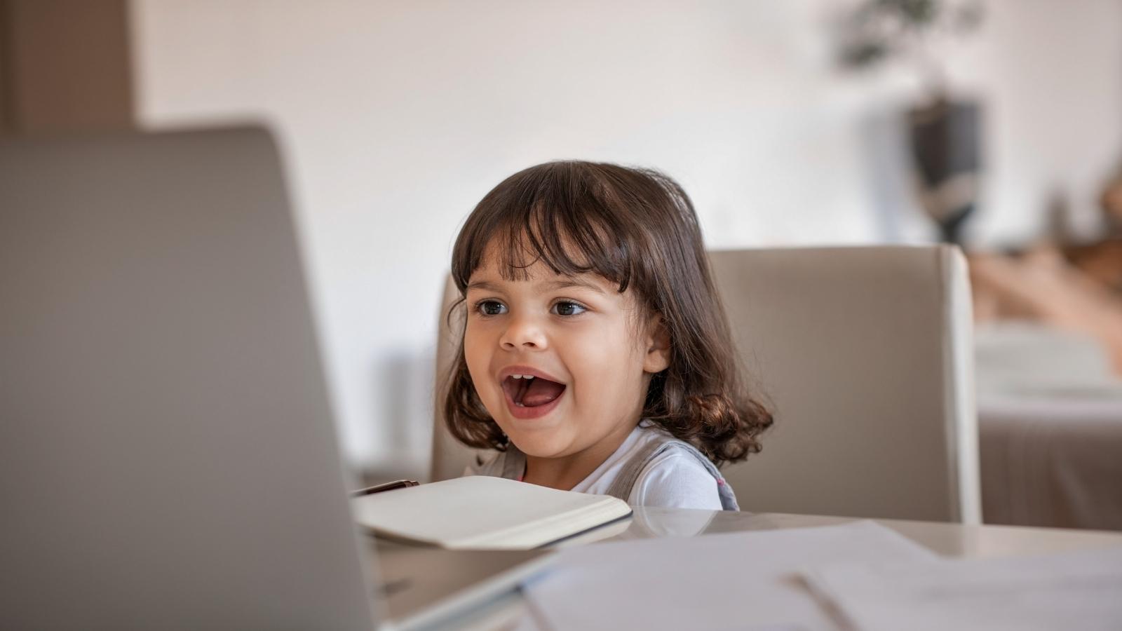 A photo of a girl sitting at a table talking into a laptop computer.