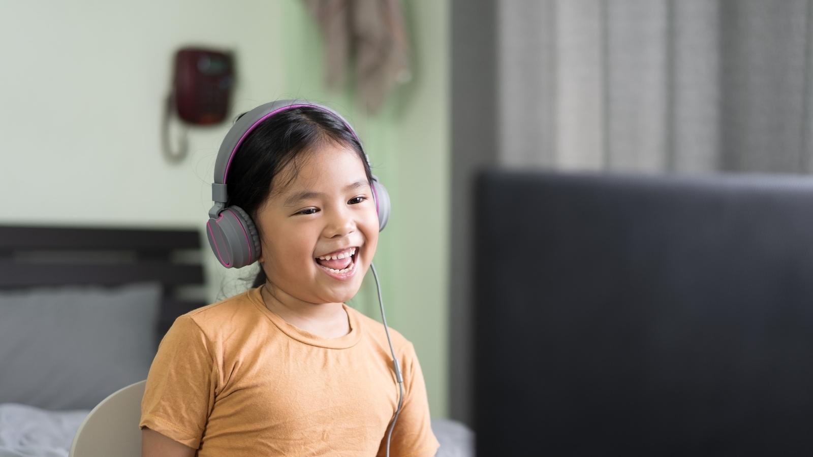 An photo of a girl sitting at a desk in her bedroom, completing a voice-enabled game on her laptop. SoapBox Labs' voice technology, which has just been recognized in Fast Company's Next Big Things in Tech 2022, powers voice-enabled experiences like these.