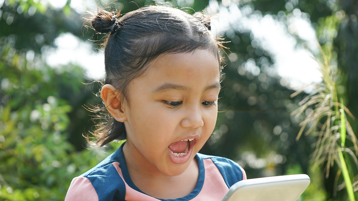 A photo of a girl standing outside, talking into a smart phone.