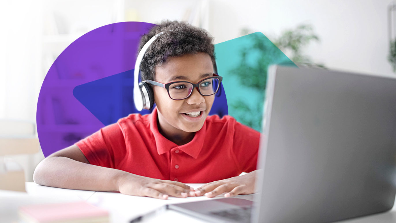 A photo of a boy wearing headphones sitting at a desk and talking into a laptop computer.