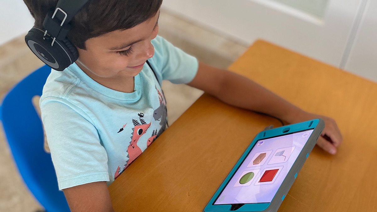 A photo of a boy sitting at a desk completing EarlyBird Education's dyslexia and early reading assessment, powered by SoapBox Lab's speech technology.