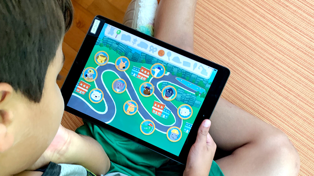 A photo of a boy sitting on the ground looking at the home screen of EarlyBird's dyslexia screener for students at the primary level.