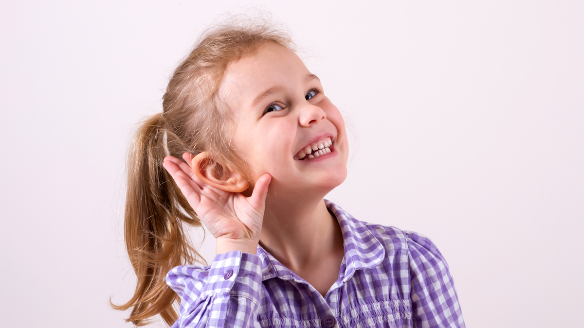 A photo of a young girl holding her right hand to her hear, showing she is listening.