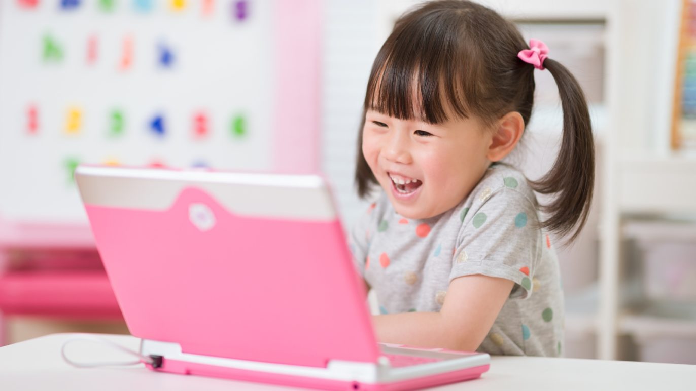 A photo of a girl sitting at a desk, completing a voice-enabled language learning lesson on her laptop computer.