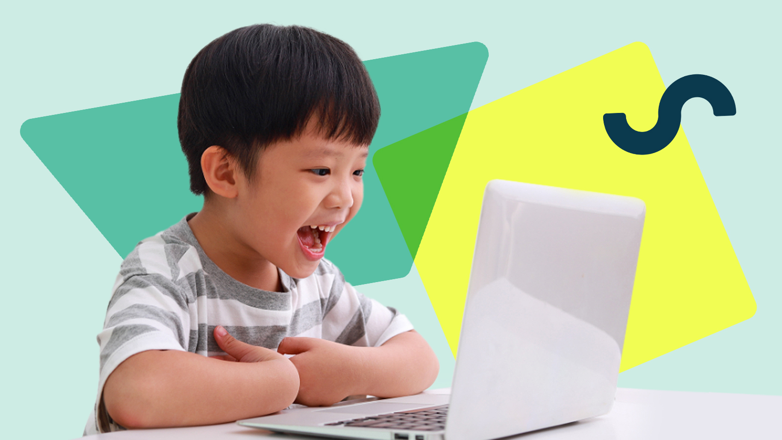 A photo of a young boy sitting at a desk talking into a laptop computer.